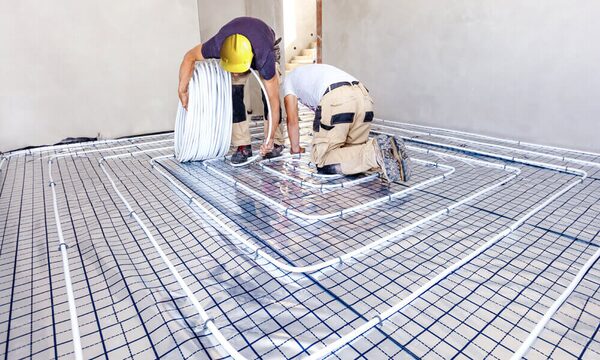 Two workers installing underfloor heating pipes over an insulated floor in a room under construction