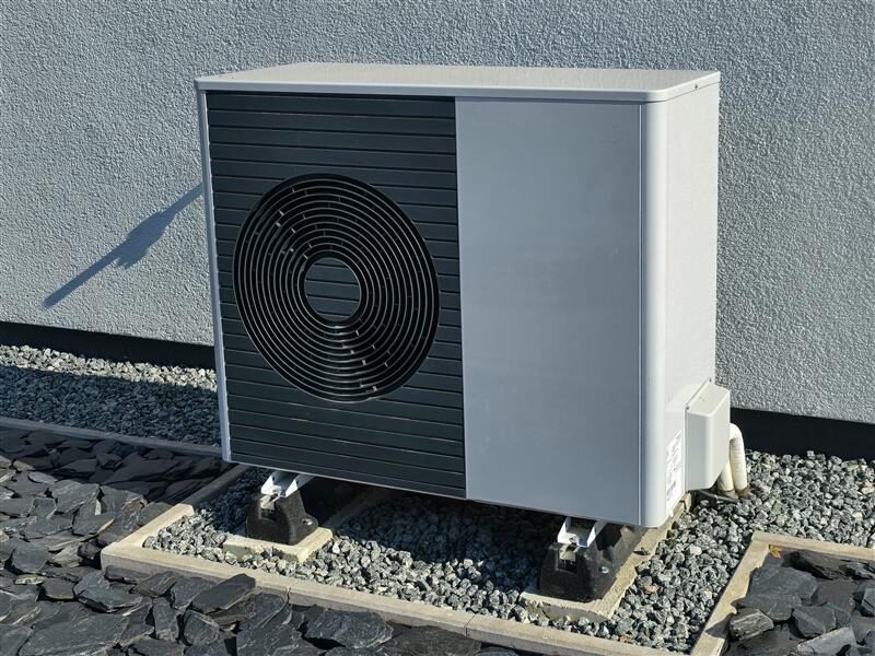 An air source heat pump unit installed outside a house on a gravel bed against a grey rendered wall