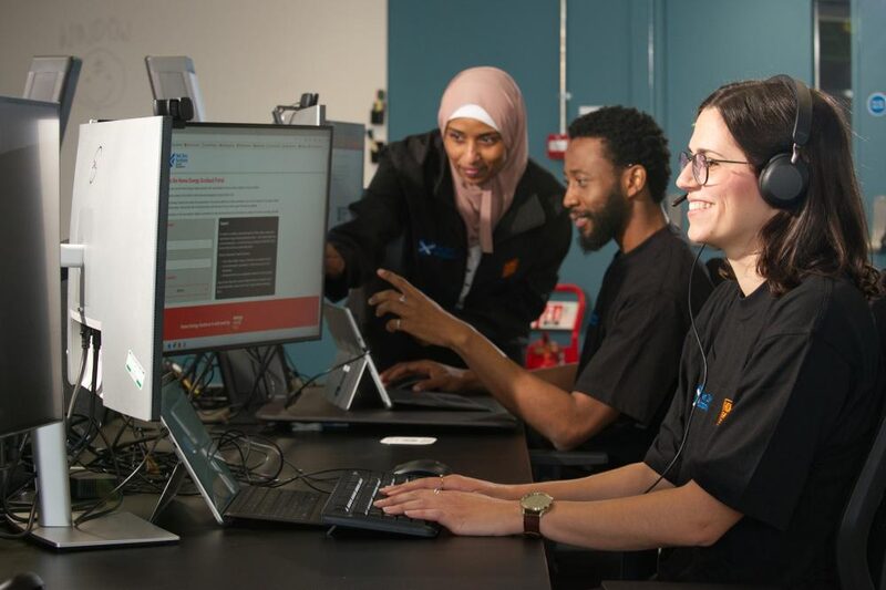 Home Energy Scotland advisers wearing headsets helping customers at computer workstations in an advice centre