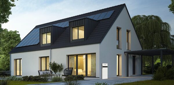 A modern house with solar panels on the roof and a white home battery storage unit mounted on the exterior wall
