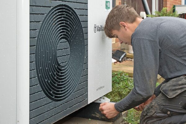 An engineer installing a Vaillant air source heat pump outside a house