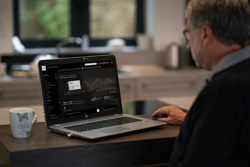 A man at a kitchen counter viewing the MCS Data Dashboard on an HP laptop