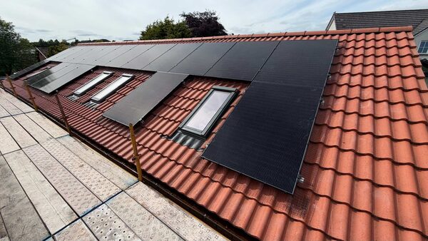 Solar panels installed on a red-tiled house roof with skylights, seen from scaffolding
