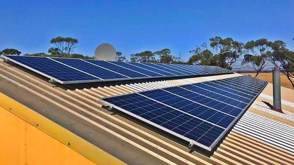 Solar panels installed on a corrugated metal roof of a rural building under a clear blue sky