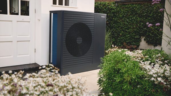A Vaillant aroTHERM pro air source heat pump unit installed outside a house next to a white door, surrounded by garden plants