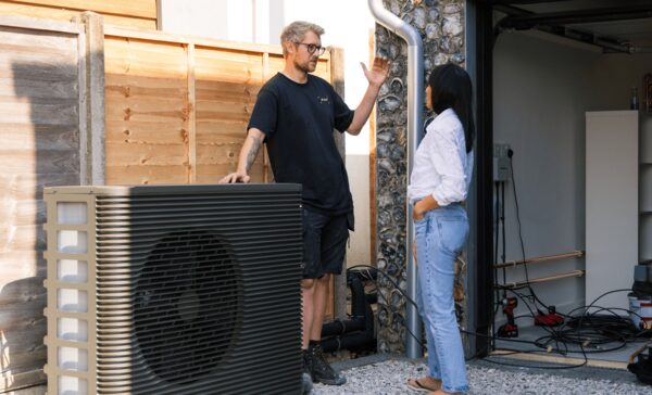 An installer talking to a woman beside an air source heat pump outdoor unit at a house during installation