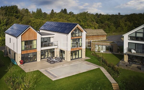 A modern house with full-roof solar panels integrated into the roof, seen from above in a garden setting