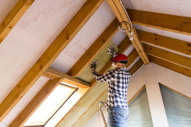 A man on a ladder fitting mineral wool insulation between the rafters of a loft