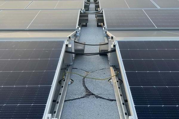 Rows of solar panels mounted on a flat roof with aluminium mounting rails and cabling