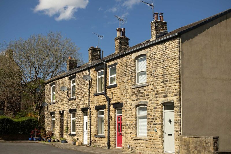 A row of traditional stone terraced houses under a blue sky, one with a smooth rendered exterior wall illustrating solid wall insulation