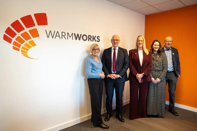 Five people standing in an office beside a Warmworks logo on the wall