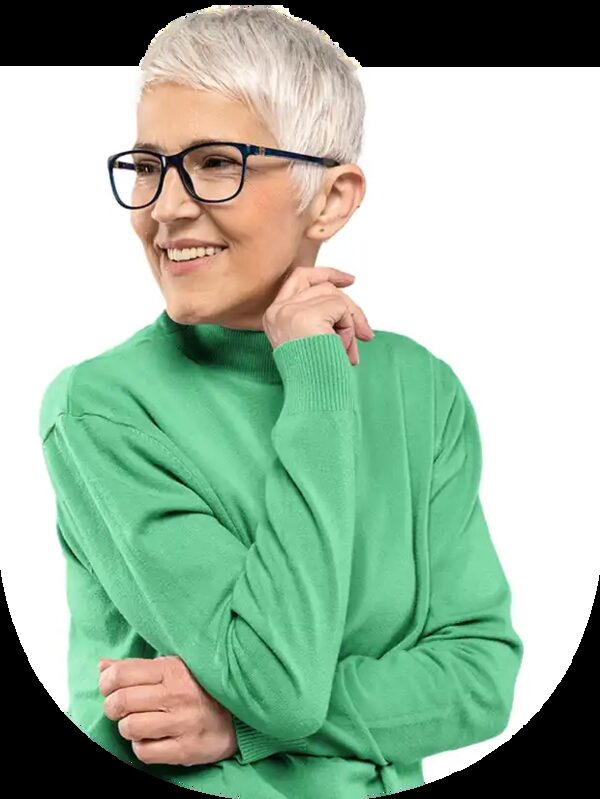 A smiling older woman with short grey hair and glasses wearing a green jumper, posed against a plain white background