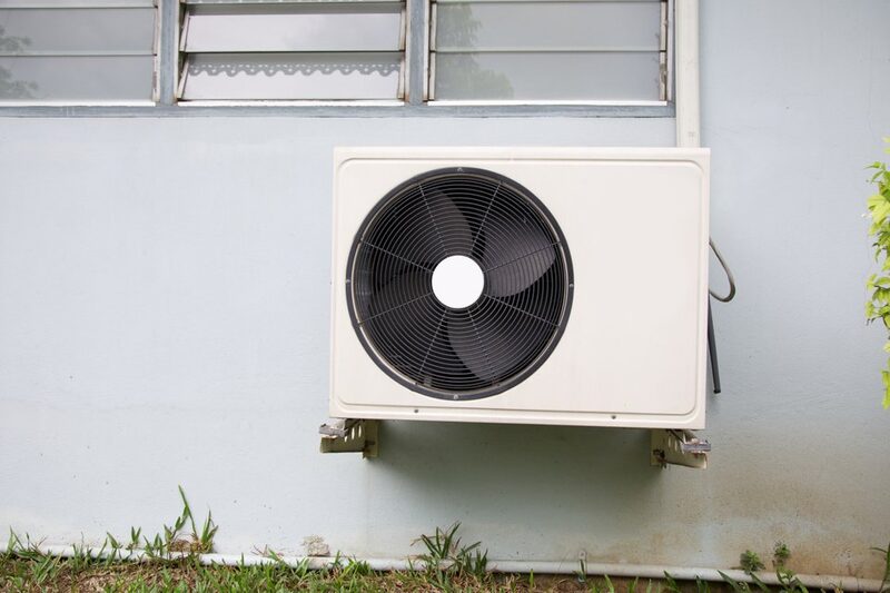 An air source heat pump outdoor unit with a large fan mounted on the exterior wall of a house
