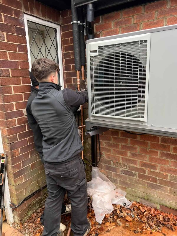 An engineer installing an air source heat pump unit on the outside wall of a brick house