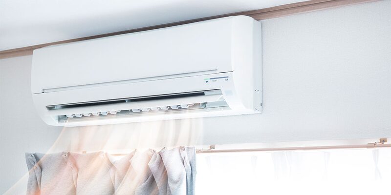 A white wall-mounted split-unit air conditioner blowing air in a room above a curtain rail