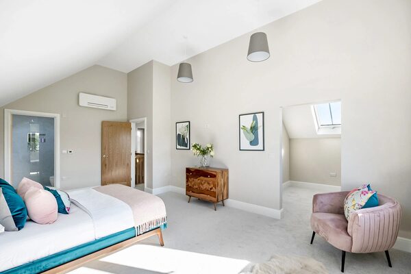 A wall-mounted air source heat pump indoor unit installed high on the wall of a bright, modern bedroom