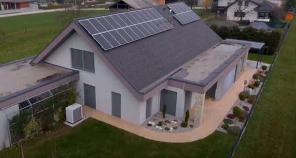 Aerial view of a modern house with solar panels on the roof and a heat pump unit beside it