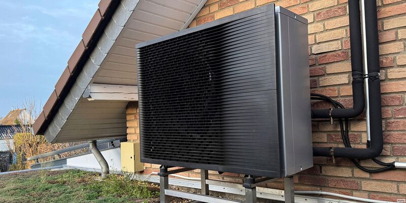 An air source heat pump unit installed on a metal frame against the brick wall of a house