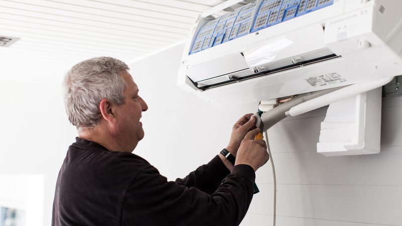 A technician installing a wall-mounted air conditioning / heat pump indoor unit, connecting the pipework