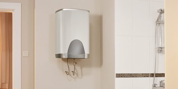 A white wall-mounted electric water heater with two pipes installed on a tiled bathroom wall next to a shower