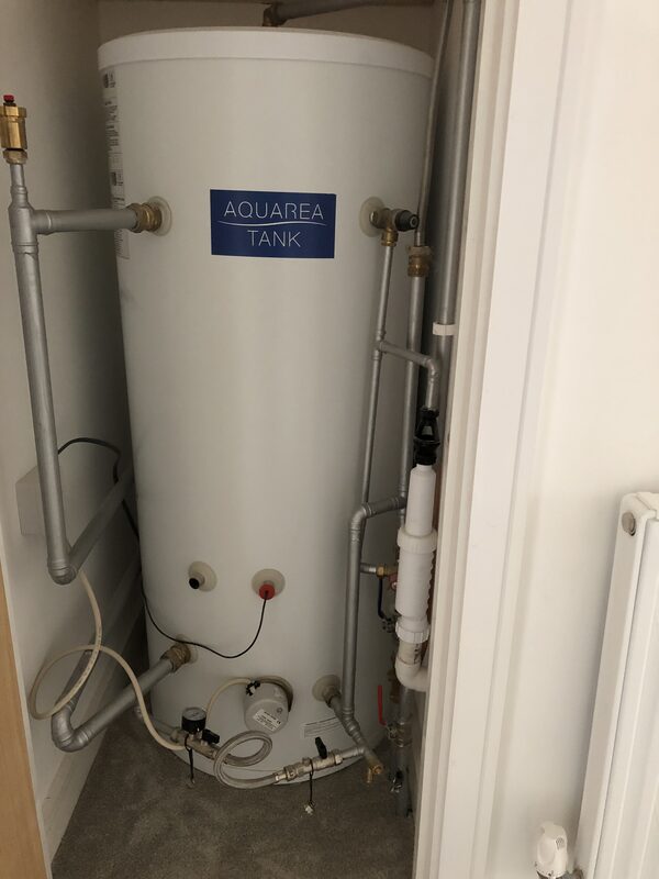 A Panasonic Aquarea hot water cylinder tank installed in a cupboard with connected pipework and valves