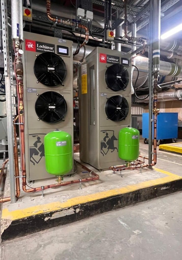 Two Lochinvar Amicus AquaStore commercial air source heat pump units installed in a plant room with copper pipework and green expansion vessels