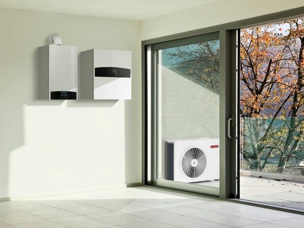 An Ariston Nimbus hybrid heat pump system with two wall-mounted indoor units and an outdoor fan unit on a balcony, seen from a bright modern room