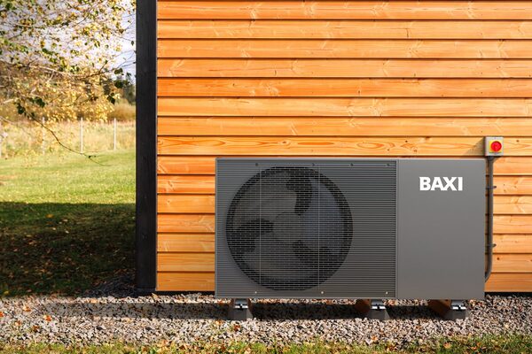 A Baxi air source heat pump unit installed outside a timber-clad building on a gravel base