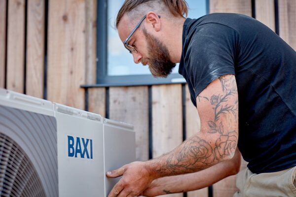 An engineer installing a Baxi air source heat pump unit outside a timber-clad building