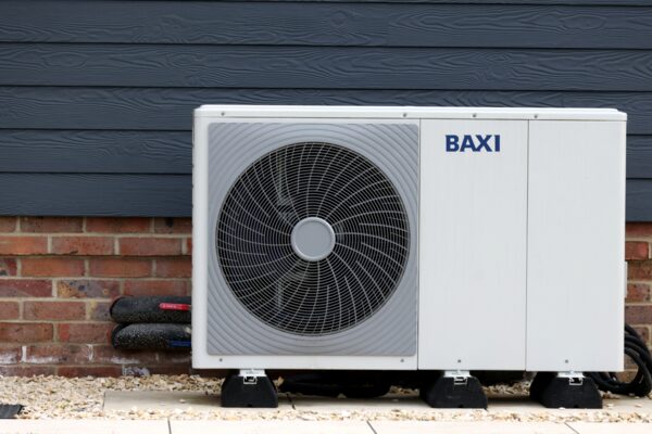 A white Baxi air source heat pump unit installed outside a house against a brick wall and dark cladding