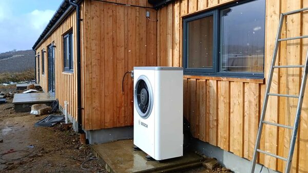 A white Bosch air source heat pump unit installed outside a timber-clad house