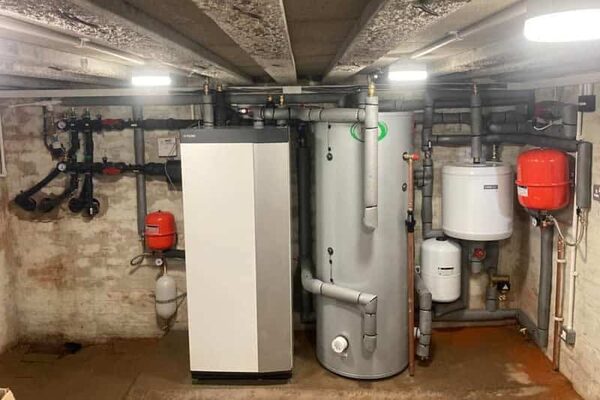 A ground source heat pump unit, hot water cylinder and buffer tank with pipework installed in a basement plant room