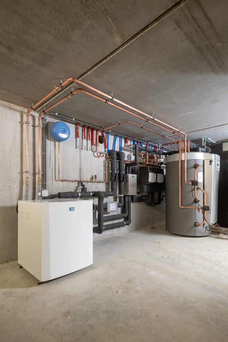 A heat pump and hot water cylinder with copper pipework and manifolds installed in a plant room