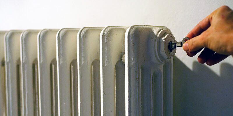 A hand using a radiator key to bleed a white column radiator against a wall