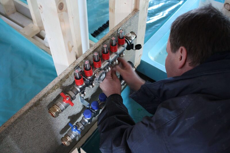 An engineer adjusting the manifold of an underfloor heating system on a building site
