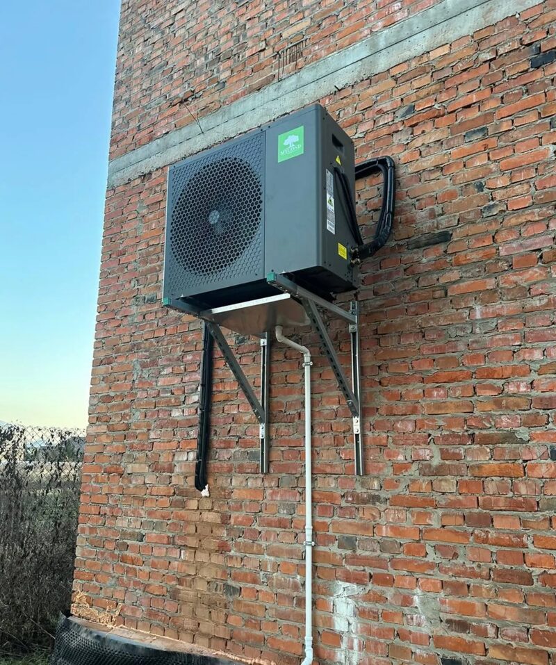 A Mycond air source heat pump unit mounted on a bracket against an external brick wall of a house