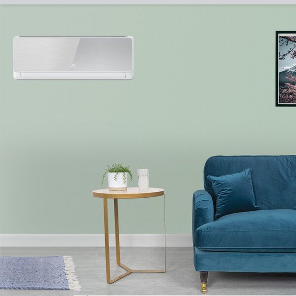 A silver electriQ wall-mounted air conditioning unit installed on a pale green living room wall above a side table and blue sofa