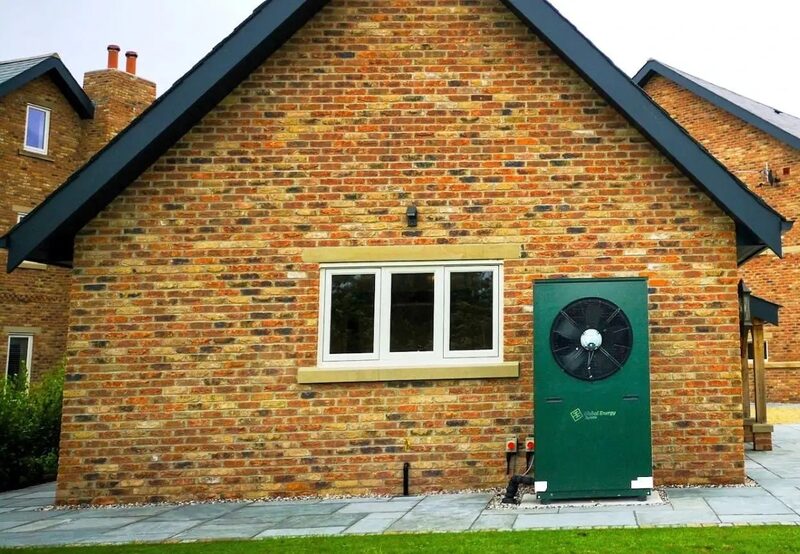 A green Global Energy Systems air source heat pump installed on the brick exterior wall of a house