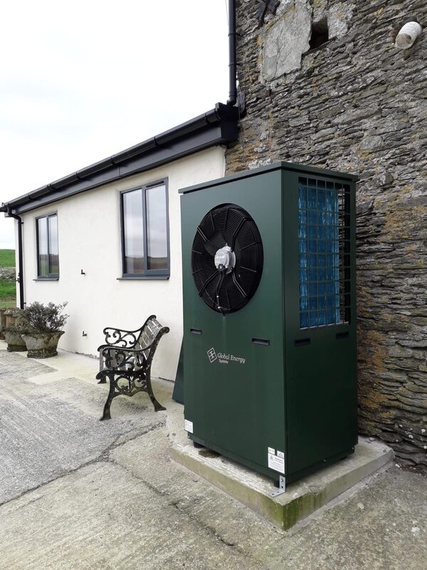 A green Global Energy Systems air source heat pump installed outside a stone farmhouse