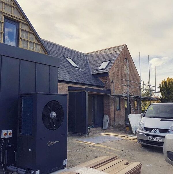 A Global Energy Systems air source heat pump installed outside a brick chapel conversion under renovation, with scaffolding and a van nearby