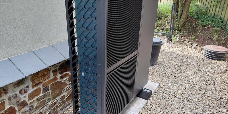 A Grant Aerona 290 air source heat pump unit installed outside a stone house on a gravelled garden area