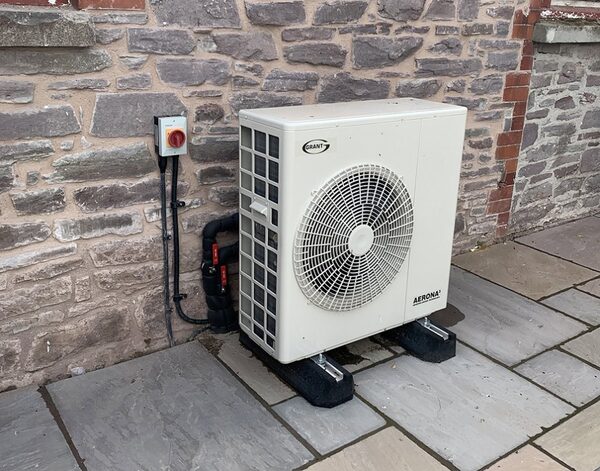 A Grant Aerona air source heat pump unit installed outside a stone house on a paved patio