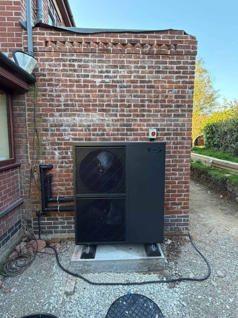 A Grant air source heat pump installed on a concrete base against a brick wall outside a house