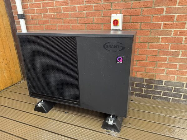 A Grant Aerona air source heat pump unit installed outside a brick house on a wooden deck