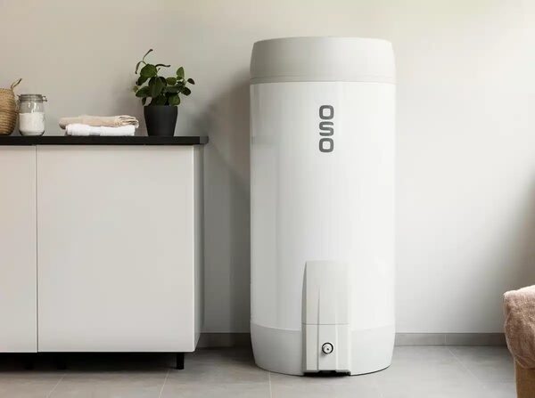 A white OSO hot water cylinder standing in a utility room next to a white cabinet