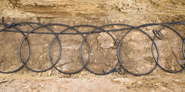 Black ground loop pipes coiled in a dug trench for a ground source heat pump installation