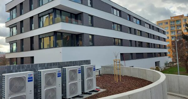 A row of Haier air source heat pump outdoor units installed beside a modern multi-storey residential apartment block