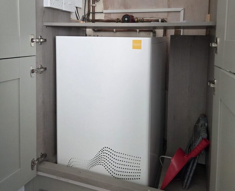 A white tepeo ZEB heat battery installed inside a kitchen cupboard with pipework above