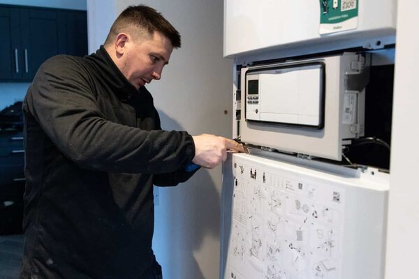 A technician installing an indoor Vaillant heat pump unit on a wall inside a home