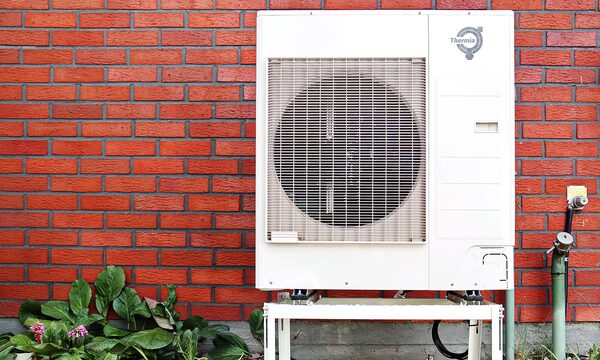 A white Thermia air source heat pump unit mounted on a stand against a red brick wall with plants below